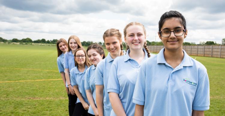 Row of school girls lined up behind each other on the playing field. 