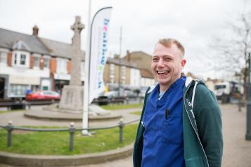 Man wearing scrubs stood in front of a Healthwatch banner