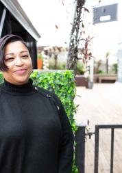 Woman wearing black stood in front of a hedge and building smiling at the camera